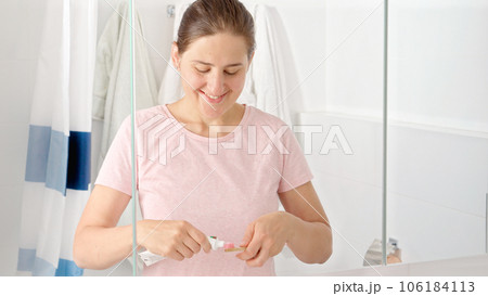 Young woman in pajamas applying toothpaste and brushing her teeth in the morning. Concept of teeth health, self checking mouth and oral hygiene. 106184113