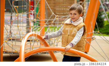 Slow motion of happy smiling boy spinning on merry-go-roud carousel at public playground. Active child, sports and development, kids playing outdoors. 106184224
