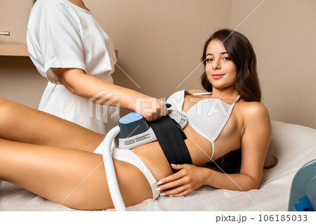 Woman puts device for body sculpting on stomach of smiling client in spa salon premise. Concept of professional work and appearance care Woman puts device for body sculpting on stomach of smiling client in spa salon premise. Concept of professional work and appearance care 106185033
