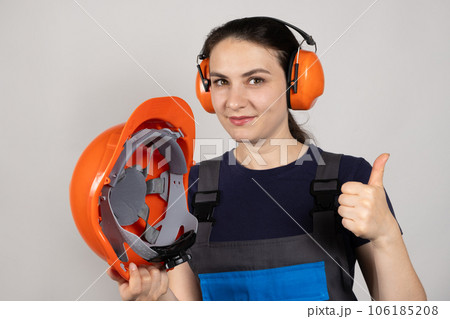 A female construction worker or engineer wearing earmuffs, headphones holds a protective helmet. Clothing for construction workers and other. 106185208