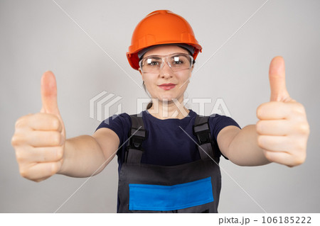 A female construction worker or engineer wearing a helmet and glasses shows thumbs up on a white background. 106185222