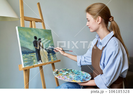 Young pretty female artist painting with acrylics on an easel Young pretty female artist painting with acrylics on an easel 106185328