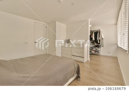 a bedroom with white walls and wood flooring, including a large bed in the center of the room is an open closet a bedroom with white walls and wood flooring, including a large bed in the center of the room is an open closet 106188679