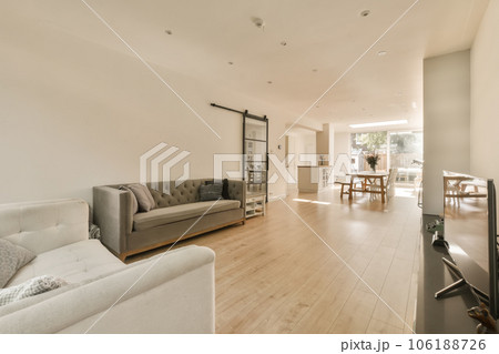 a living room with white walls and hardwood flooring in the center of the room, there is a grey couch on the right a living room with white walls and hardwood flooring in the center of the room, there is a grey couch on the right 106188726