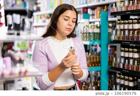 Satisfied young woman chooses and tries perfume in cosmetics store Satisfied young woman chooses and tries perfume in cosmetics store 106190576