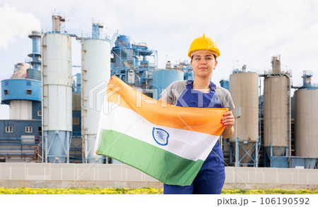 Happy girl in work clothes and hardhat with flag of india standing in front of industrial scenery Happy girl in work clothes and hardhat with flag of india standing in front of industrial scenery 106190592