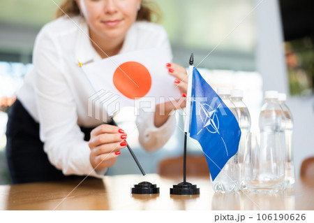 Employee of delegation prepares negotiating table - sets up flag of NATO (OTAN) and Japan 106190626