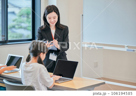 小学生の生徒の勉強を見守る若い塾講師 106194585