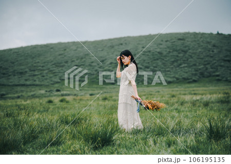 草原の中でブーケを持ってる白いワンピースの女性 106195135