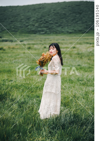 草原の中でブーケを持ってる白いワンピースの女性 106195140