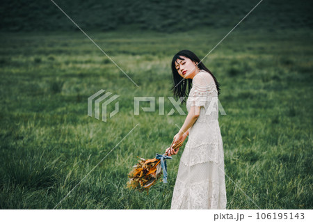 草原の中でブーケを持ってる白いワンピースの女性 草原の中でブーケを持ってる白いワンピースの女性 106195143