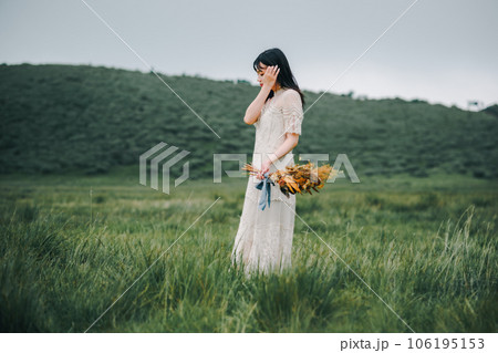 草原の中でブーケを持ってる白いワンピースの女性 106195153