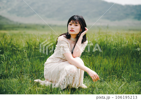 草原にしゃがんでいる白いワンピースを着た女性 106195213