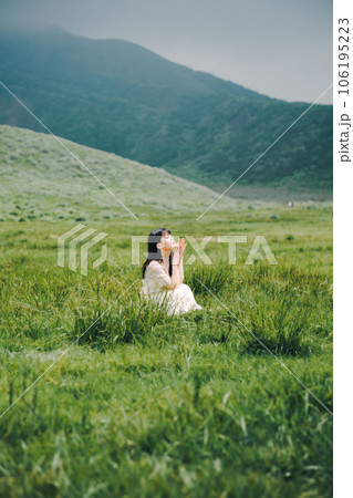草原にしゃがんでいる白いワンピースを着た女性 106195223