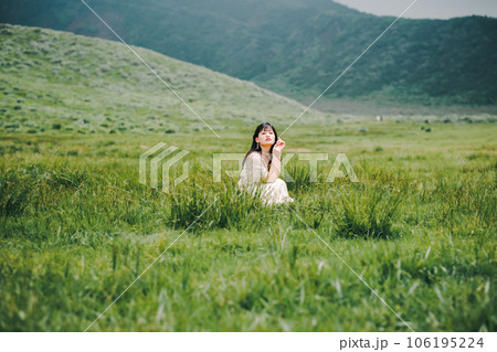 草原にしゃがんでいる白いワンピースを着た女性 106195224