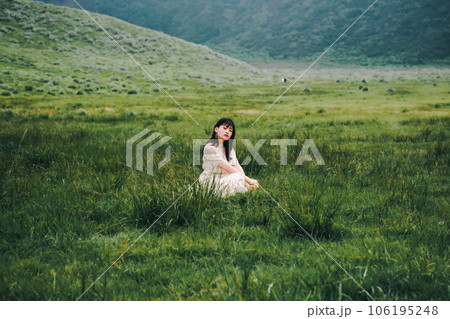 草原にしゃがんでいる白いワンピースを着た女性 106195248