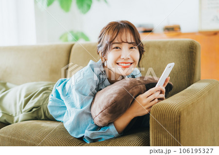 ソファに寝転がってスマホを持つ女性 106195327