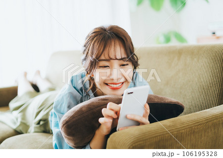 ソファに寝転がってスマホを見る女性 106195328