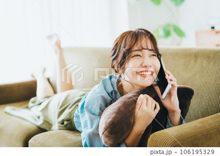 ソファに寝転がって電話をする女性 106195329