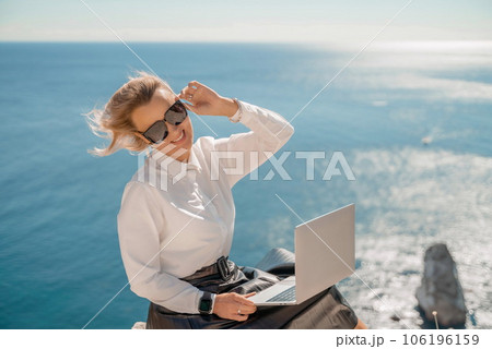 Business woman on nature in white shirt and black skirt. She works with an iPad in the open air with a beautiful view of the sea. The concept of remote work. Business woman on nature in white shirt and black skirt. She works with an iPad in the open air with a beautiful view of the sea. The concept of remote work. 106196159