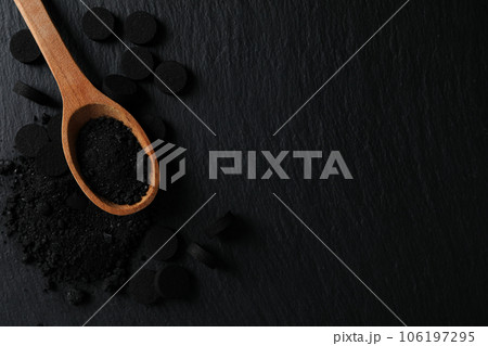 Activated charcoal powder in a wooden spoon on a dark background 106197295
