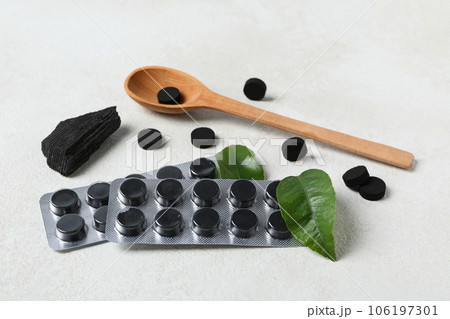 A wooden spoon with activated charcoal tablets and leaves 106197301