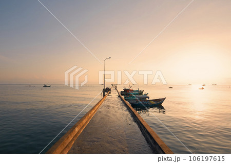 Long pier with moored boats in fishing village at sunrise. Long pier with moored boats in fishing village at sunrise. 106197615