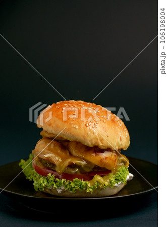 Close-up of a delicious fresh homemade burger with lettuce, cheese, onion and tomato on a rustic wooden board on a dark background Close-up of a delicious fresh homemade burger with lettuce, cheese, onion and tomato on a rustic wooden board on a dark background 106198004