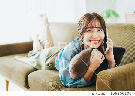 ソファに寝転がって電話をする女性 106200100