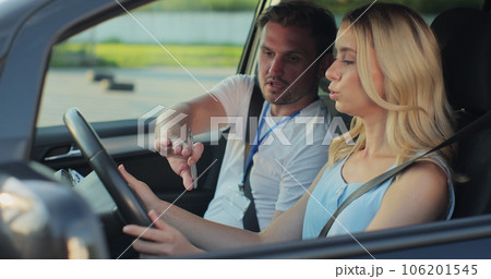 Young woman and driving school instructor with clipboard talking in car. Woman listening to instructor in car learning to drive. 106201545