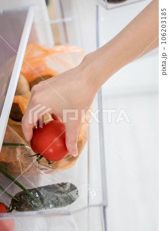 a woman's hand takes a red tomato from the refrigerator 106203185