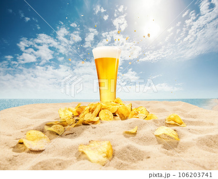 Glasses of foamy, chill, lager beer with chips appetizers on sand against ocean and blue sky background Glasses of foamy, chill, lager beer with chips appetizers on sand against ocean and blue sky background 106203741