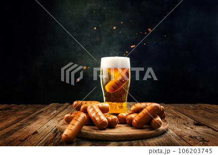 Glass with delicious, foamy, chill lager beer with grilled sausages on wooden table over dark background 106203745
