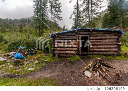 A house of logs with name - running deer - in the mountains for overnight stays during transitions. Backpacks in a heap are nearby. Mountains with forest in the fog in the background. Horizontal. 106206169