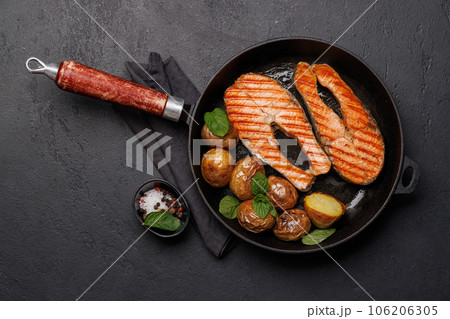 Grilled salmon steaks and potatoes sizzling in a frying pan 106206305