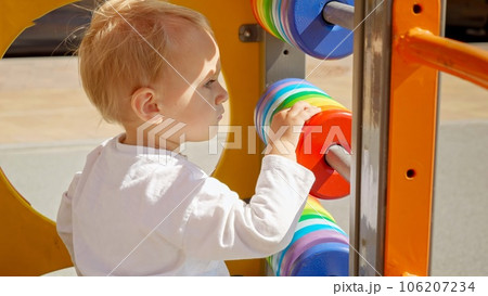 Portrait of blonde baby boy playing on colorful wooden playground outdoors. Children developments, kids education, baby learning. 106207234