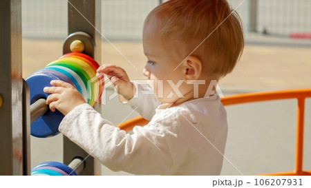 Portrait of little boy spinning colorful circles on abacus at playground. Children developments, kids education, baby learning. 106207931
