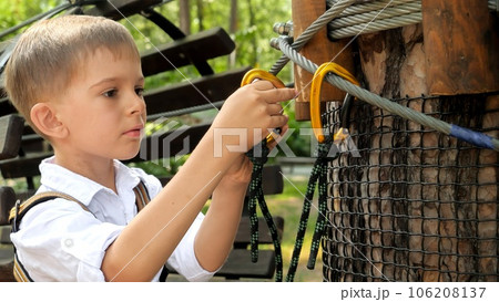 Little boy clamping his safety hook on the rope before climbing on tree at adventure park Little boy clamping his safety hook on the rope before climbing on tree at adventure park 106208137