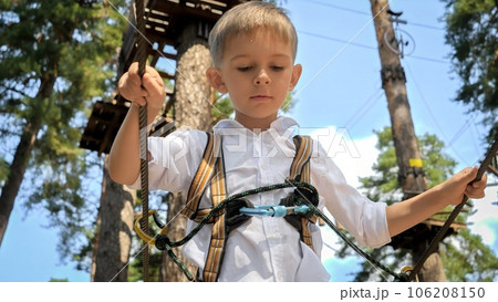 Little boy looking down while walking over wooden rope bridge in extreme adventure park Little boy looking down while walking over wooden rope bridge in extreme adventure park 106208150