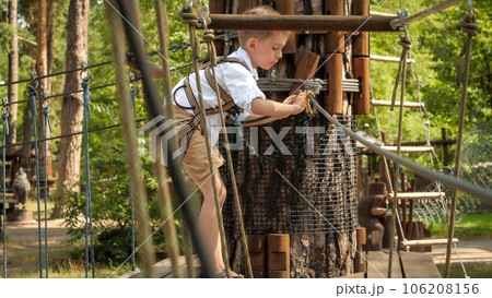 Little boy climbing over ropes and bridges in summer scout camp. Active childhood, healthy lifestyle, kids playing outdoors, children in nature. Little boy climbing over ropes and bridges in summer scout camp. Active childhood, healthy lifestyle, kids playing outdoors, children in nature. 106208156