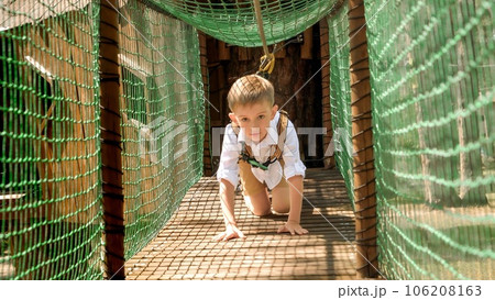 Little boy crawling on all fours over wooden bridge at rope adventure park. Active childhood, healthy lifestyle, kids playing outdoors, children in nature. Little boy crawling on all fours over wooden bridge at rope adventure park. Active childhood, healthy lifestyle, kids playing outdoors, children in nature. 106208163