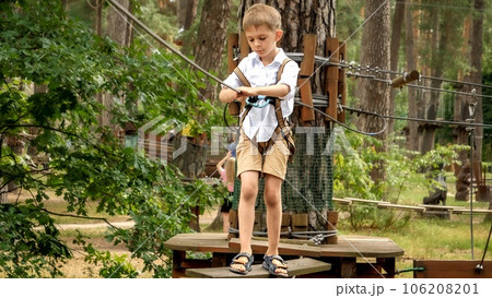 Little concentrated boy lookin down his feet while crossing wobbly rope bridge in extreme park Little concentrated boy lookin down his feet while crossing wobbly rope bridge in extreme park 106208201
