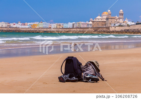 Two backpacks, a hat and sandals lie on the sand on the coastline against the backdrop of the sea. Two backpacks, a hat and sandals lie on the sand on the coastline against the backdrop of the sea. 106208726