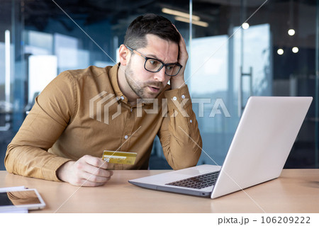 Problems with payment, credit card transaction. A young man sits in the office in front of a laptop monitor and anxiously holds his head. 106209222