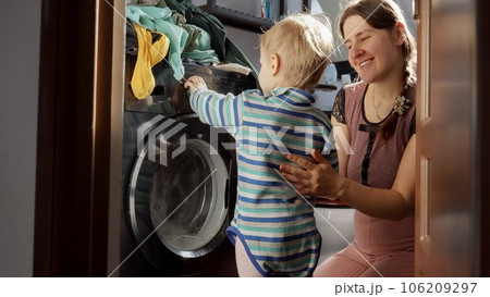 Little baby boy helping mother doing laundry in washing machine. Doing housework and chores, children education and development. 106209297