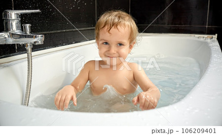Baby boy's joy is cheerful as he splashes water playfully, creating a refreshing spray and filling the bathroom with laughter Baby boy's joy is cheerful as he splashes water playfully, creating a refreshing spray and filling the bathroom with laughter 106209401