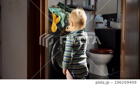 Little baby boy pressing knobs and buttons on working washing machine. Doing housework and chores, children education and development. 106209409