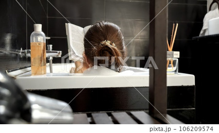 Rear view of elegant woman relaxing in bath with interesting book. Self-care, education, hygiene and spa. Rear view of elegant woman relaxing in bath with interesting book. Self-care, education, hygiene and spa. 106209574