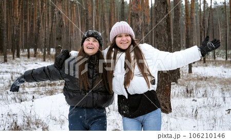 Two laughing teenage girls cheering and laughing while catching falling snowflakes in winter forest 106210146
