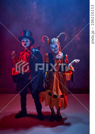 Trick or treat. Boy and girl, children wearing costumes for halloween, standing with basket for candies against dark background in neon light with smoke Trick or treat. Boy and girl, children wearing costumes for halloween, standing with basket for candies against dark background in neon light with smoke 106210153